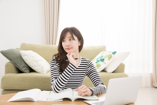 パソコンと資料を並べながら悩んでいる女性