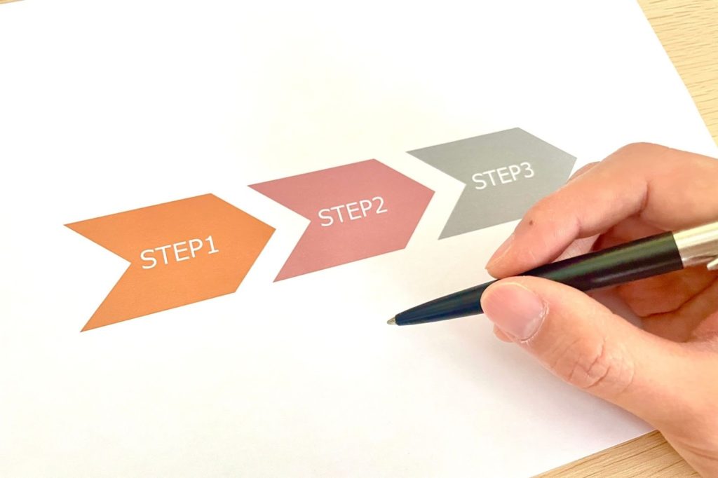 STEP1・STEP2・STEP3と書かれた矢印型の図を前に、ペンを持った手が指し示している