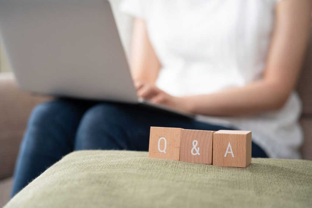 ソファに座ってノートパソコンを操作する人の前に、Q&Aと印字された木製ブロックが置かれている