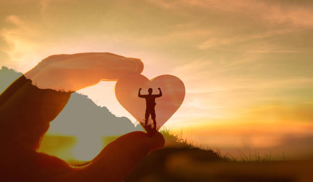 中央に人、ハートがあり、ハートを左手で持っているような画像。背景は山と夕焼け空で、すべてが透けて重なっている。