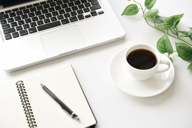 パソコンとコーヒーとノートがデスクの上に置いてある