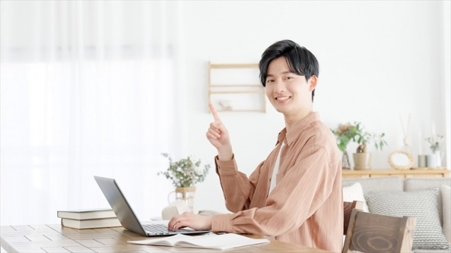ノートパソコンを操作しながら人差し指を指す男性