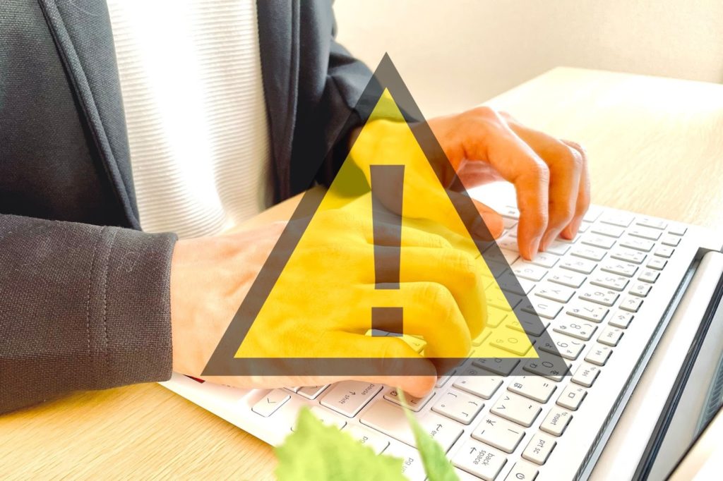 パソコンを操作する男性と注意を示すマーク