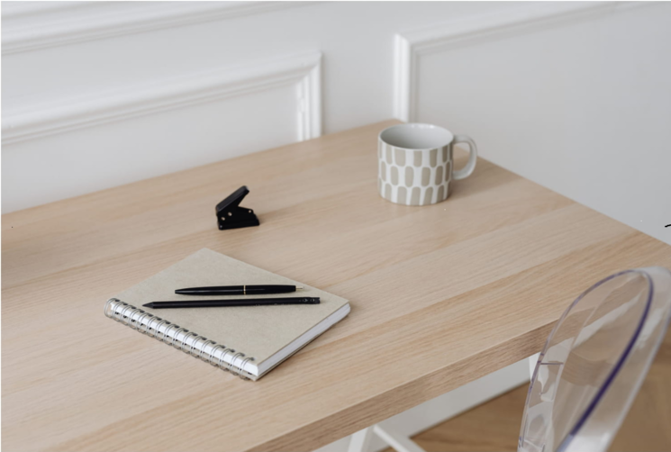 デスクにノートとペン、マグカップが置いてある