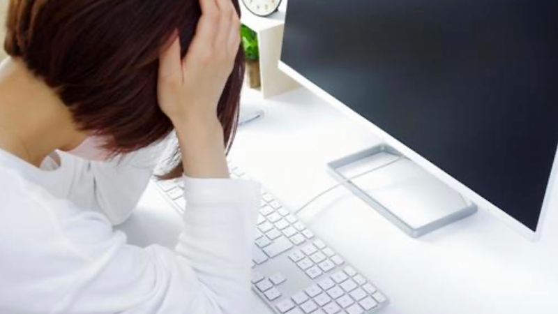 パソコンの前で頭を抱える女性の後ろ姿