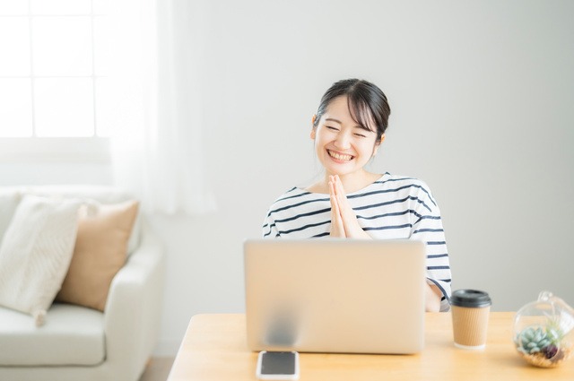 ノートパソコンの前で手を合わせて喜んでいる女性
