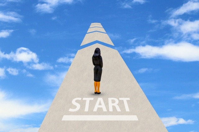青空の中央に道が通っていて、STARTと書かれているところに女性が立っている