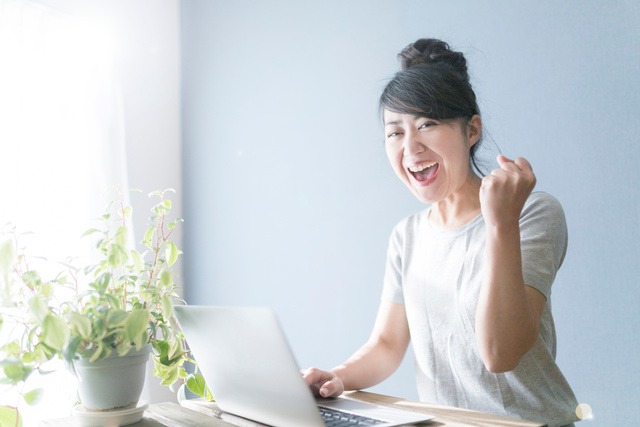 女性がパソコンの前で笑顔でガッツポーズしている