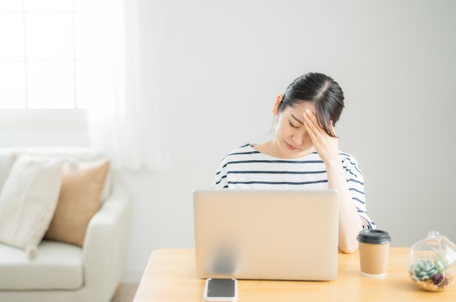 パソコンの前で額に手をあて困った様子の女性