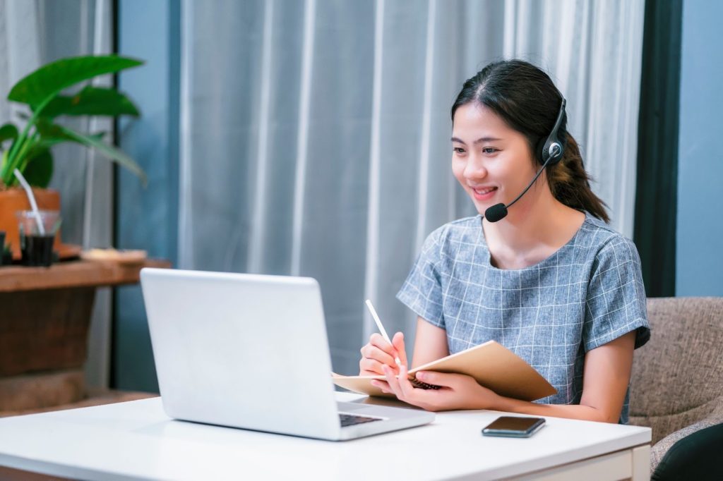 ヘッドホンマイクを付けてノートパソコンの画面を見ている女性