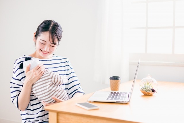 赤ちゃんをあやしながらパソコンの前に座る笑顔の女性