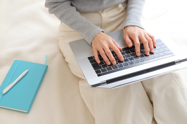 女性が膝の上にノートパソコンを置いてキーボードを打っている