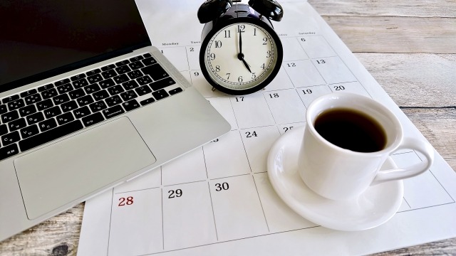 テーブルに、ノートパソコン、コーヒー、時計、カレンダーが置かれている