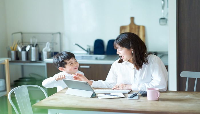 ママがテーブルでパソコン作業をしているときに、子どもがパソコンを指さして聞いている