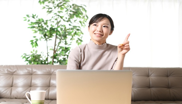 女性がパソコンを操作しながら、人差し指で何かひらめいた様子