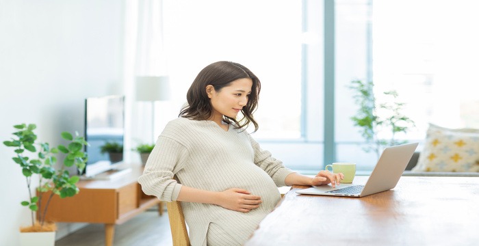 妊婦がノートパソコンを見て微笑んでいる