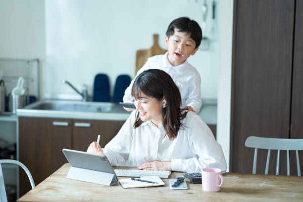 女性がダイニングテーブルでタブレットを操作している。後ろから子どもが画面をのぞき込んでいる。