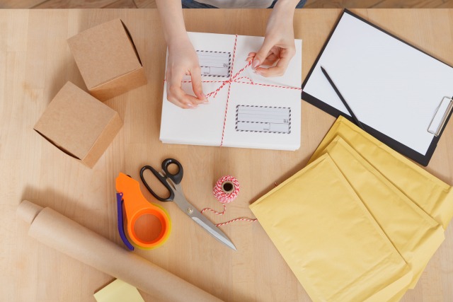 机の上で梱包作業をする手元　リボンを結ぶところを上から見ている