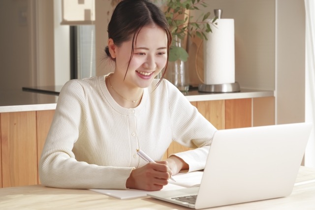 PCを開き、ノートにメモをする笑顔の女性
