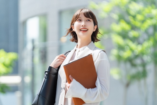 女性の会社員がノートパソコンとバッグを持って微笑んでいる