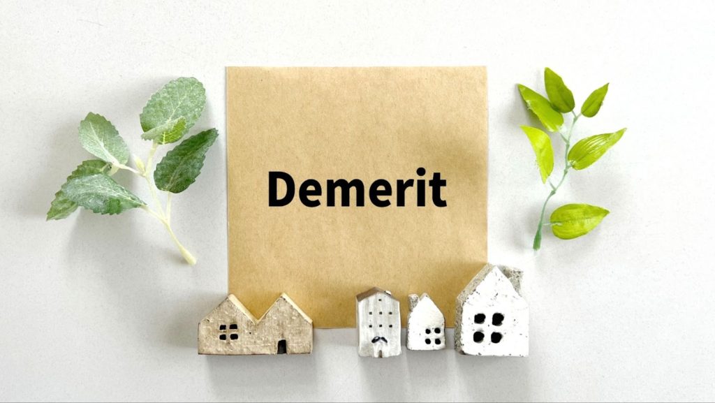 画面中心にDemeritと書いてある箱があり、両脇に葉っぱ（左・深緑、右・黄緑）の装飾がされている。Meritと書いてある箱の下方に三角屋根のオブジェが装飾されている。