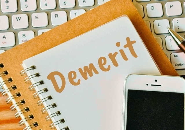 PCキーボードの上に置かれた「Demerit」と書かれたノートとスマホ